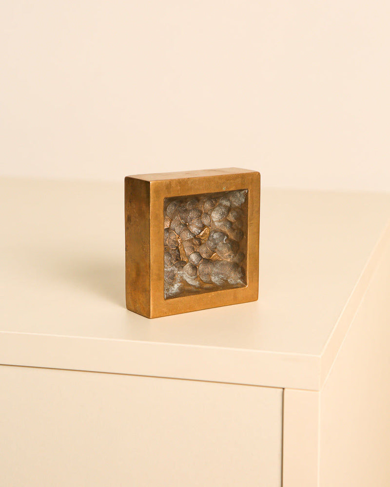 Bronze square ashtray with stones displayed on minimal surface
