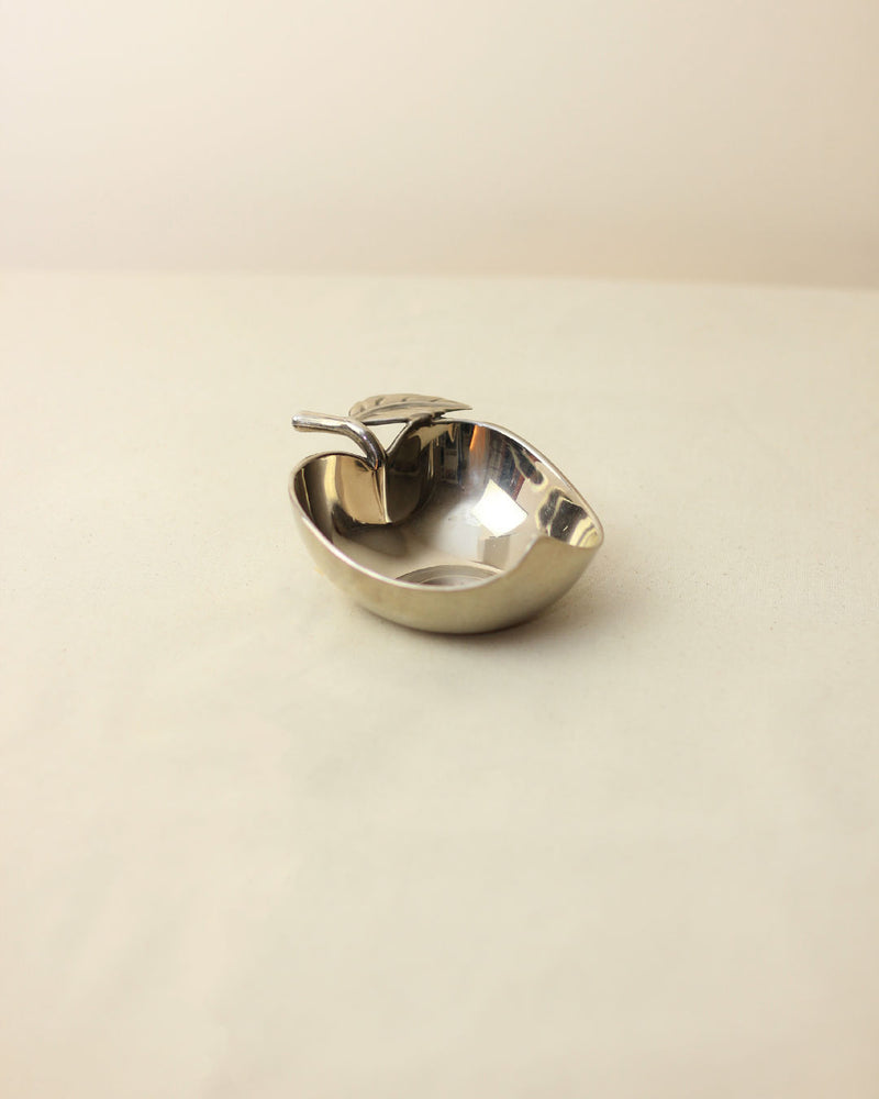 The Boga Avante Shop Decorative Apple Shaped Dish features a shiny finish with a stem and leaf detail, displayed on a simple, light-colored surface.
