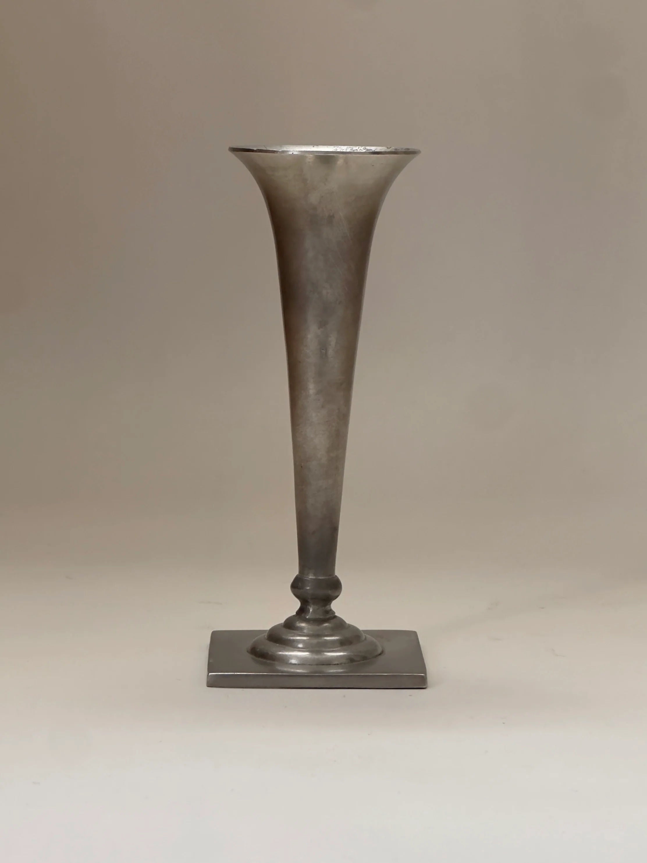 The Just Andersen vase by Galerie Storm is a pewter, tall, slender piece featuring a flared top and square base in Art Deco style, displayed against a neutral backdrop.