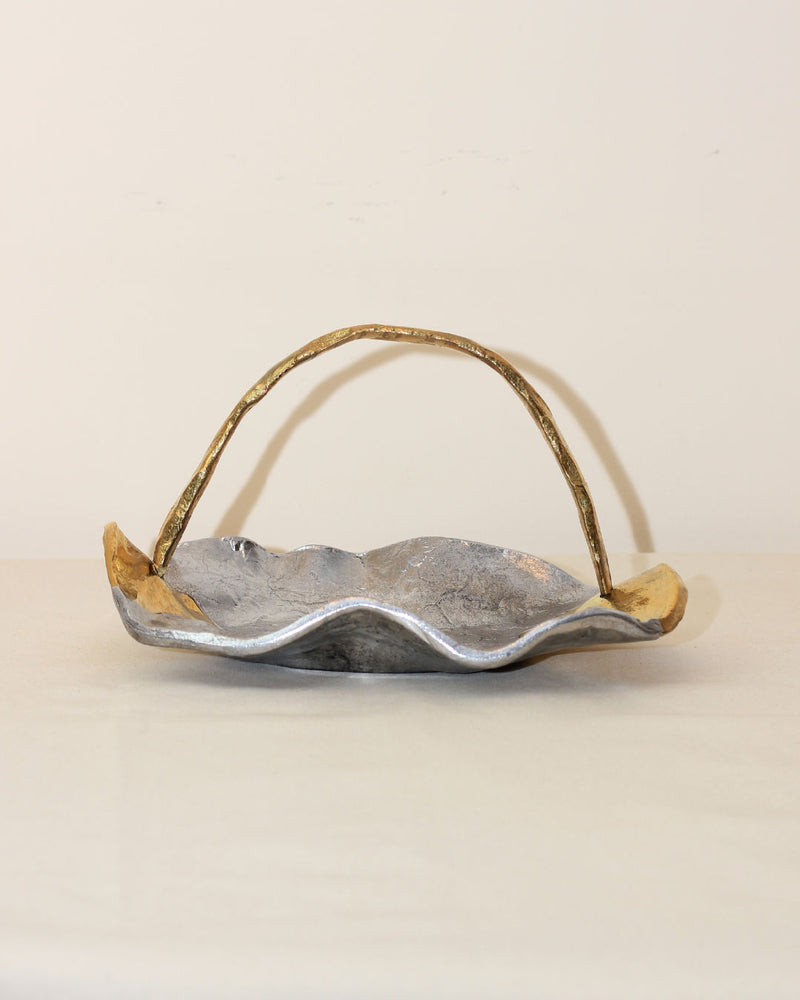 The Boga Avante Shop Brutalist Decorative Bowl pairs beautifully with a wavy-edged silver tray featuring gold accents and a curved, textured gold handle, creating a refined yet rustic display against a plain background.