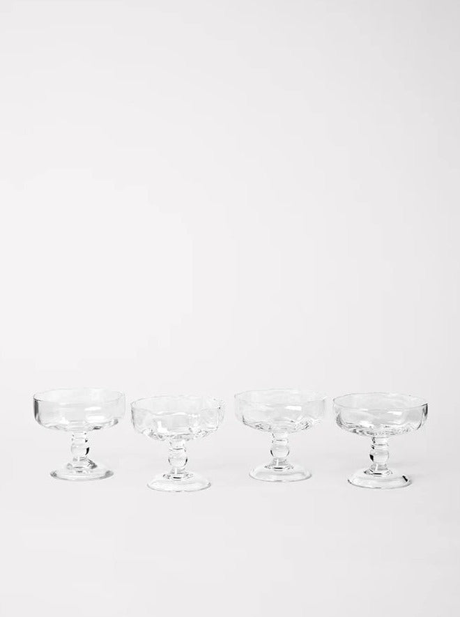 Five empty Akua Objects Alban Champagne Glasses in a row against a bright white background. Each glass features a unique, intricate design on its stem and base.