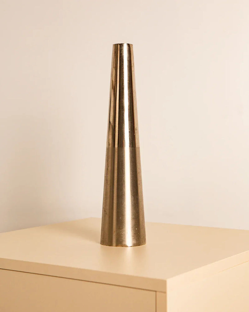 The Treaptyque Metal Cone Vase 80s, with its sleek minimalist design and a hint of vintage charm, sits on a light wooden table against a plain background, enhancing the retro decor.