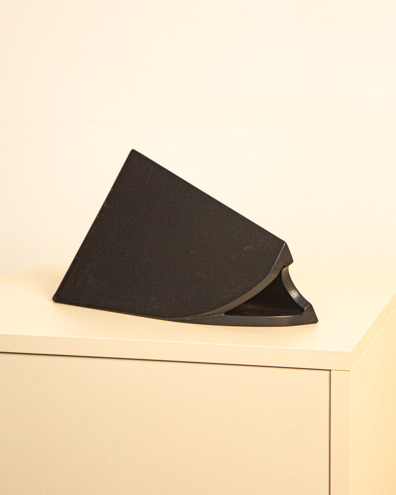 The Treaptyque “Triangle” Vase from the 1980s, an Italian black, wedge-shaped design with a curved side, sits on a beige cabinet against a light wall.