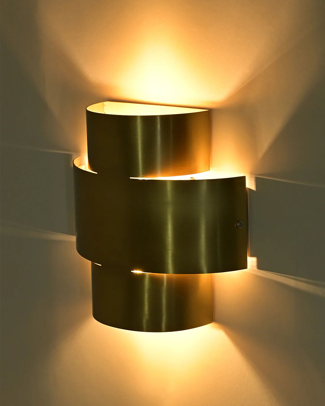 The Aura Wall Sconce by LMNOH, with a gold metallic brass finish, emits warm, diffused light. Its design of curved overlapping panels adds a stylish touch to contemporary interiors.