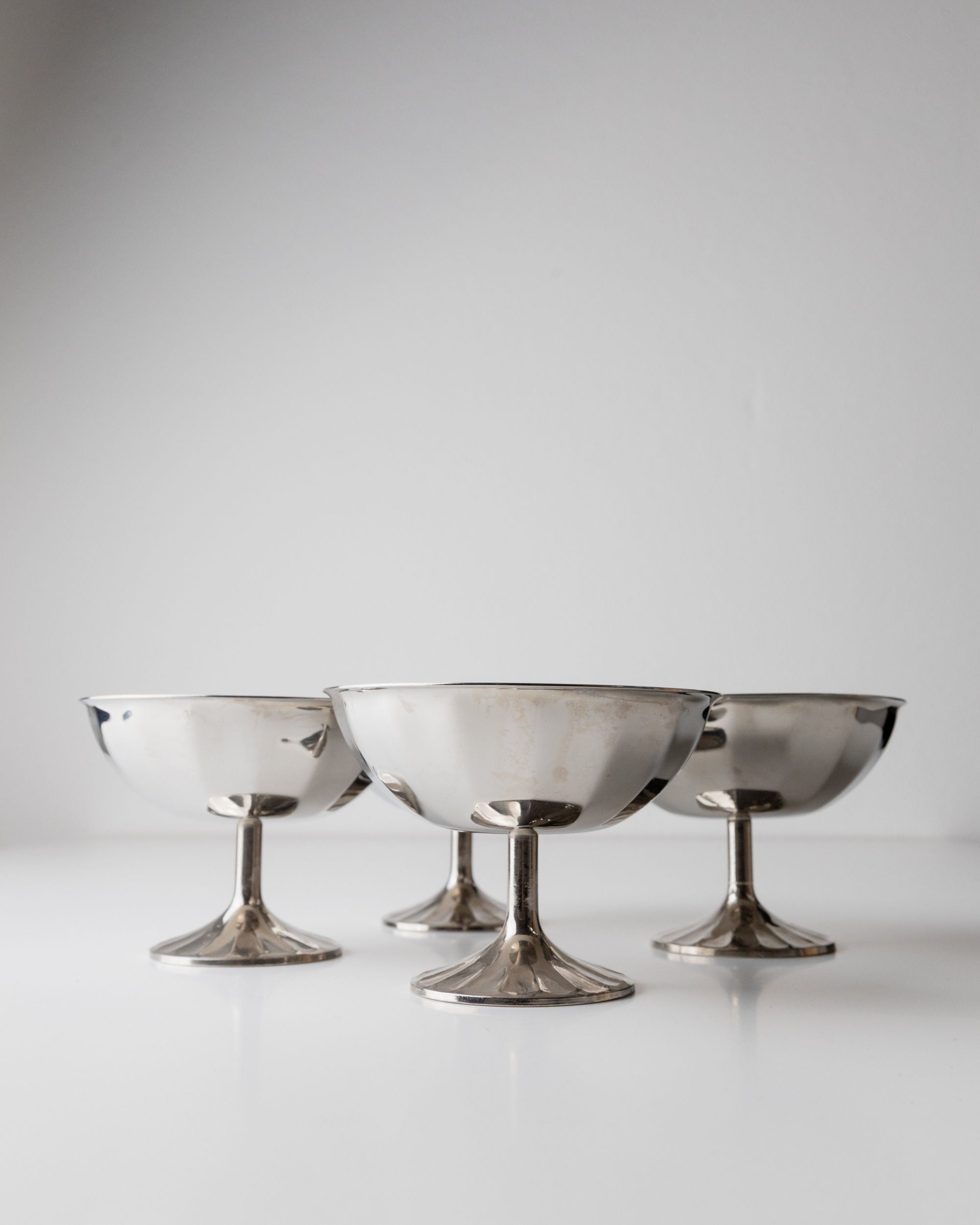 Four Bottega Jacobs Champagne Coupes from Italy, 1970s, meticulously polished in silver-plated elegance, stand with graceful stems on a pristine white surface against a plain background.