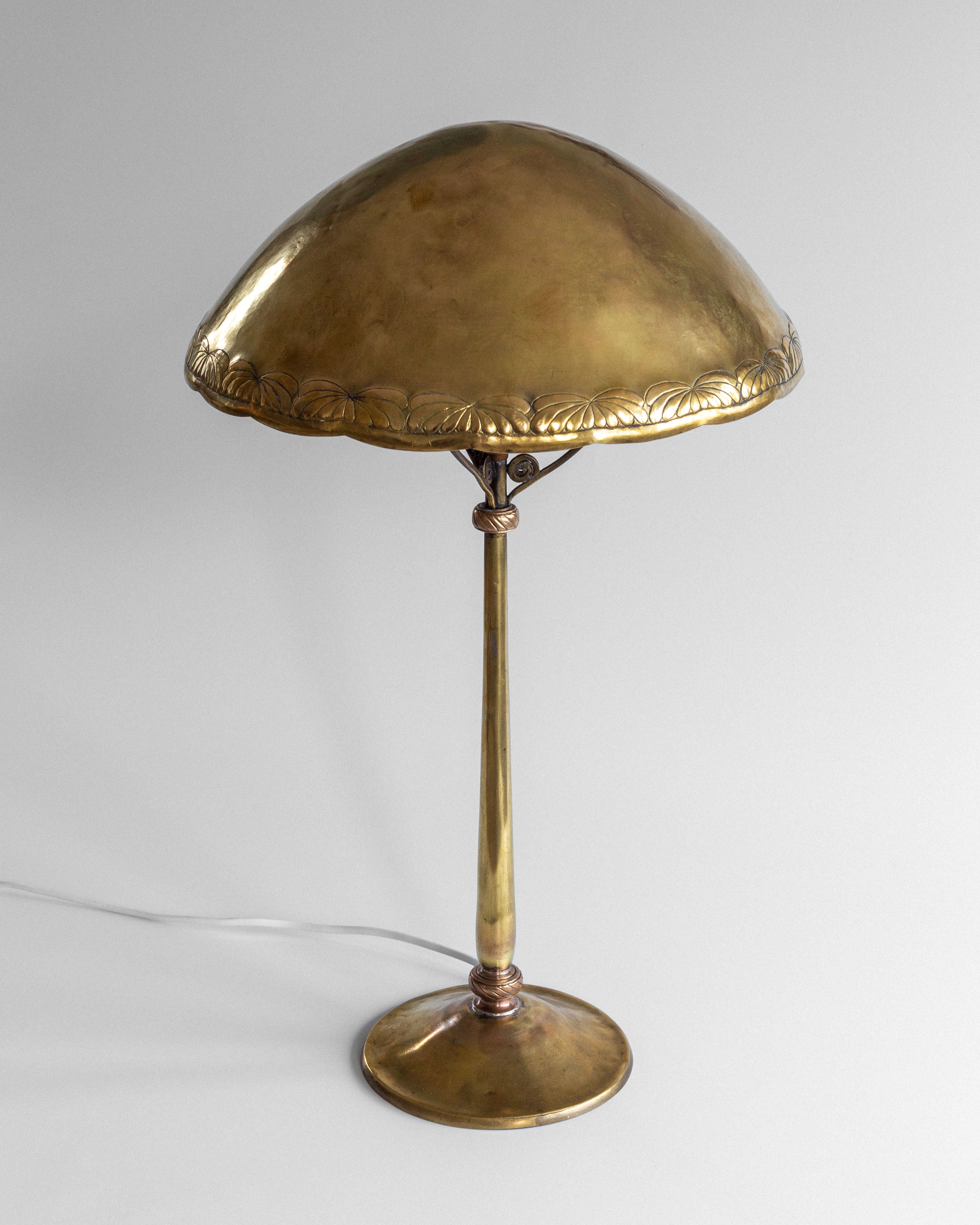 The Spigel Art Nouveau Brass Table Lamp features a vintage design with a dome-shaped shade, ornate edge detailing, a slender stem, and a round base, all in polished brass against a plain backdrop.