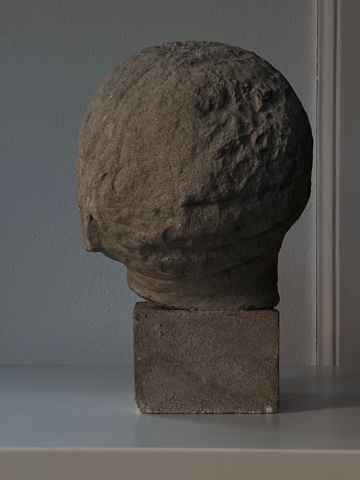 The Decorative Bust by Médecine features a textured, spherical design with a subtle patina, elegantly perched on a square base and showcased on a white surface against a neutral background.