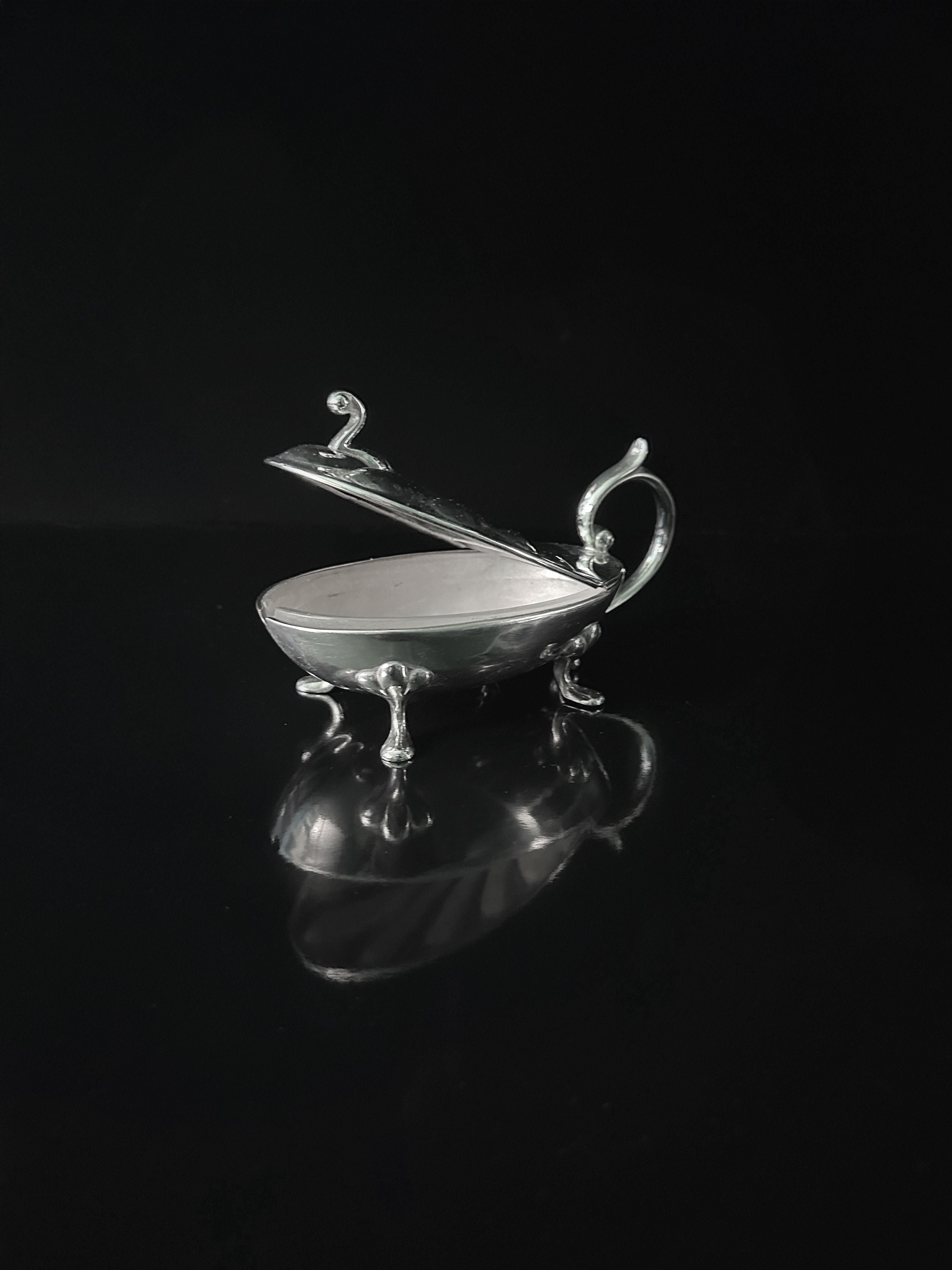 The Dodo Vintage Silver-plated Caviar Frog from the 1950s is an elegant, decorative container with a hinged lid and ornate handle, standing on three small legs. Resembling a classic caviar container, it beautifully reflects light against a dark background.