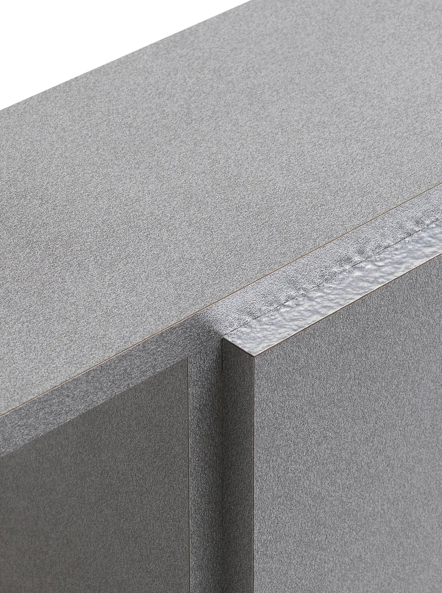 A close-up of the corner of the "Mara T" Side Table in Silver Noise by TEGET showcases a textured, layered surface similar to laminated furniture. The perspective highlights its sharp edges and smooth finish, accentuating the table's industrial look.