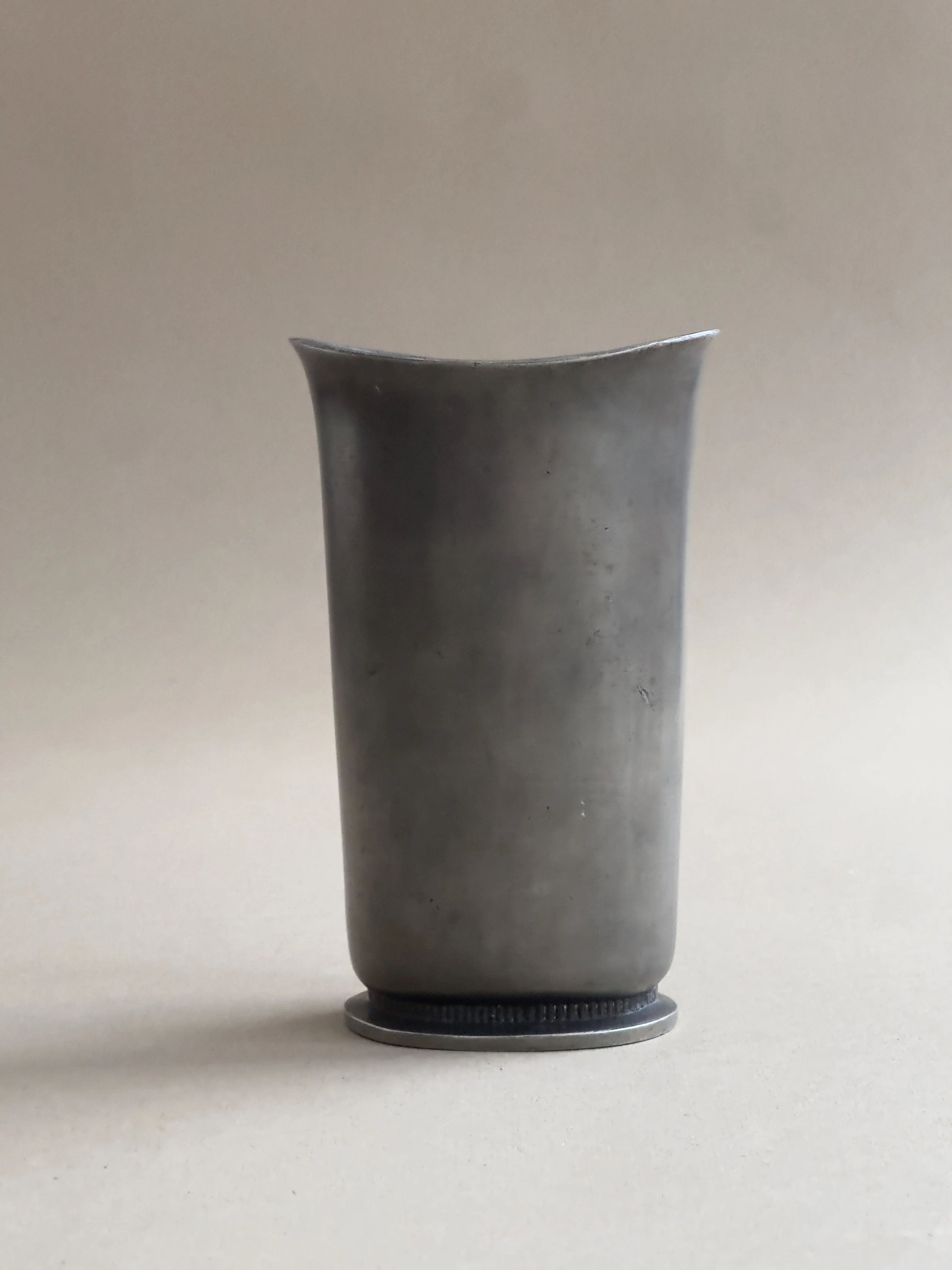 A tall, plain, cylindrical Art Deco vase in cast pewter by Galerie Storm features a slightly flared lip against a neutral background. It has a small base and an unadorned surface, evoking the timeless elegance of Swedish Grace vases.