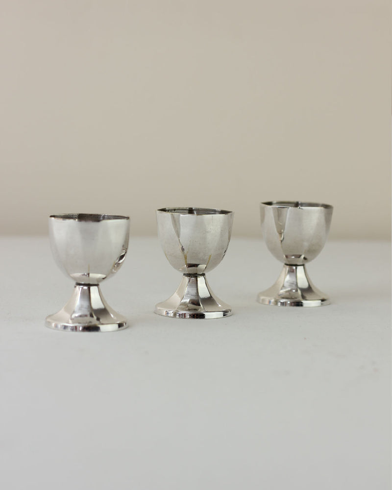 Three vintage silver-plated egg cups arranged on white surface