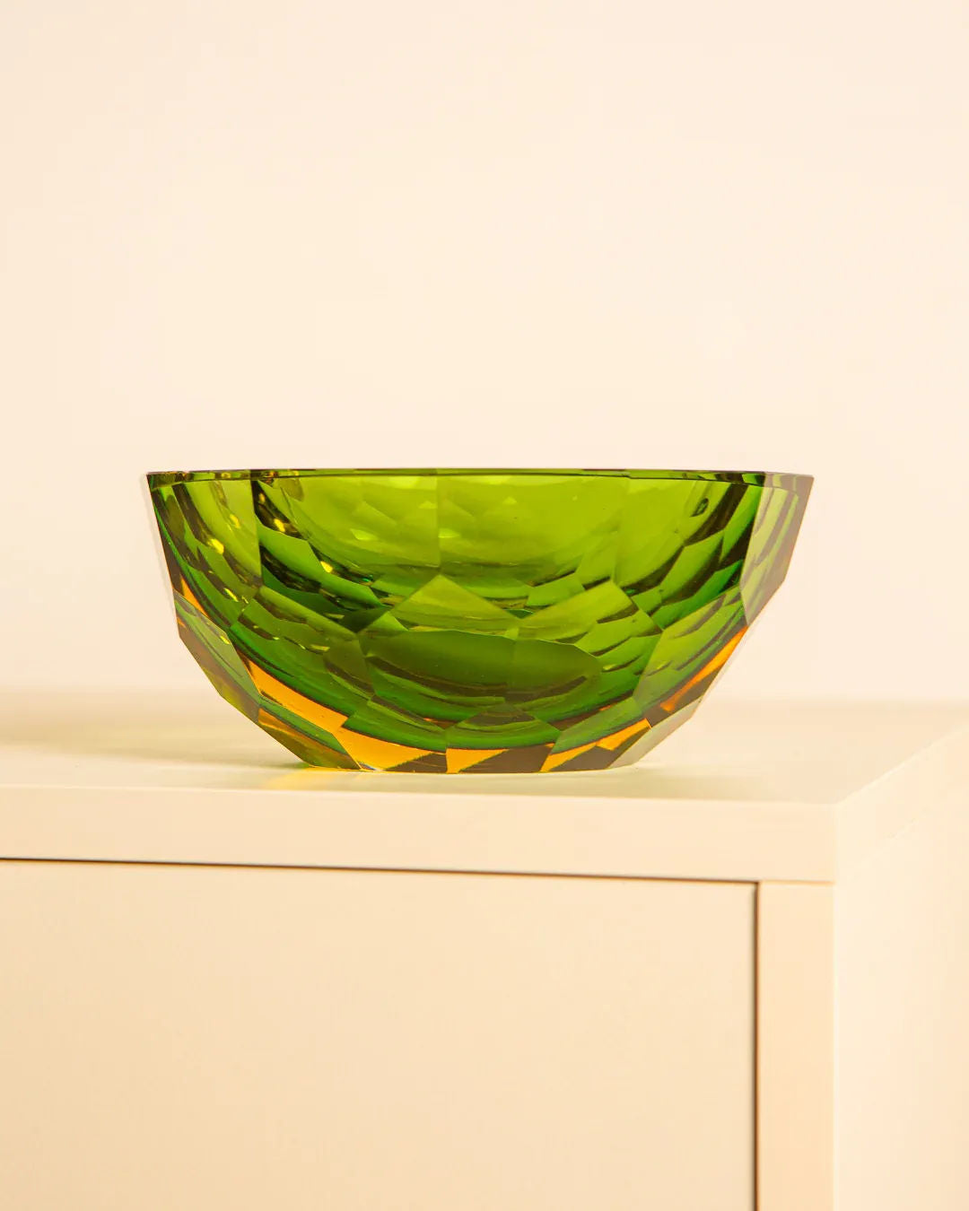 A vibrant green, faceted Murano glass bowl from Treaptyque's Large “Diamant” Vide-poches by Flavio Poli sits on a light surface against a neutral background, reflecting light and forming geometric patterns reminiscent of the iconic 1980s Italian design.