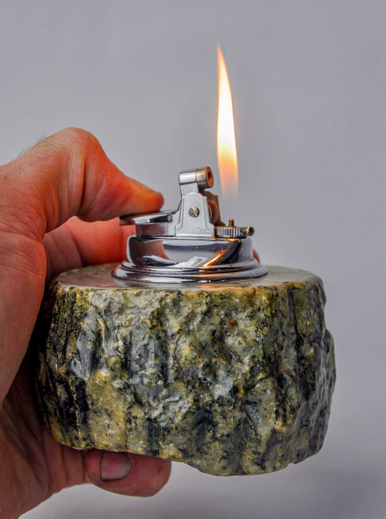 Hand holding lit green alabaster lighter showing flame and texture detail