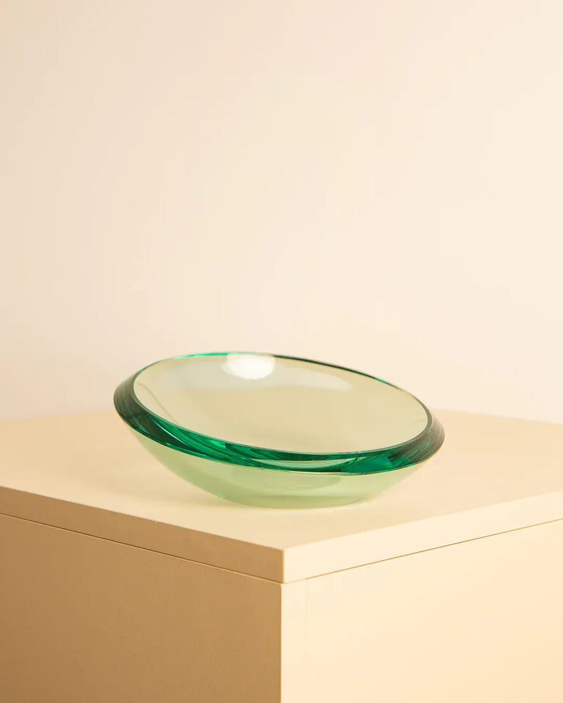 A Large Circular Vide-Poches by Fontana Arte 60's from Treaptyque, with an elegant, curved design, is placed on a light beige surface against a cream-colored background. The simplicity and minimalism of the scene highlight the vide-poches' graceful shape.