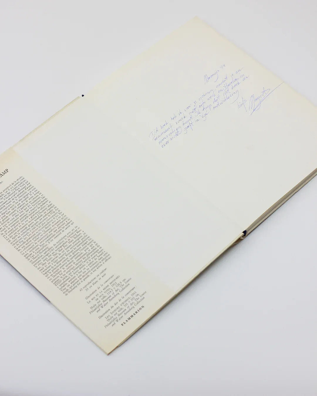 An open copy of "Marcel Duchamp" by Sarane Alexandrian, featuring text on the left page and a handwritten message on the right, captures the spirit of conceptual art. The image is set against a plain white background, echoing Marcel Duchamp's minimalist style, and is available at Boga Avante Shop.