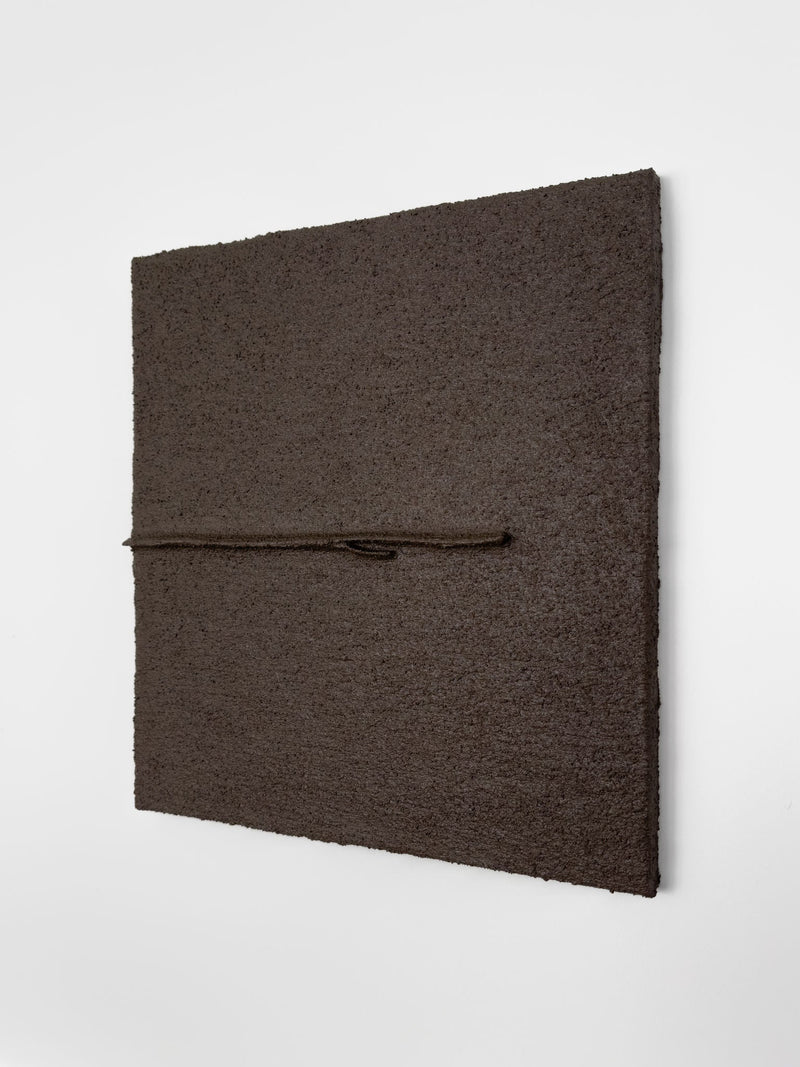 Shadow World 03" by Delal Salazar is a textured, dark brown square artwork with acrylic and sand on canvas. Mounted on a white wall, it features a thin brown cord embedded off-center, enhancing the piece's three-dimensional depth.