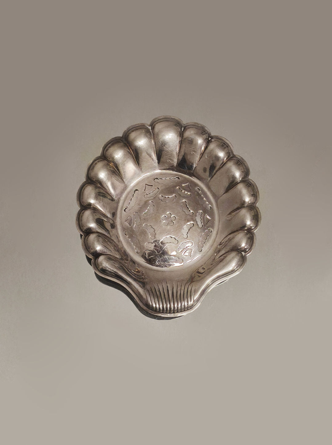 The Shell Butter Dish by Les Objoies features a silver-plated, scalloped shell design with engraved floral patterns on the interior. It's perfect for presenting delicate butter curls against a plain background.