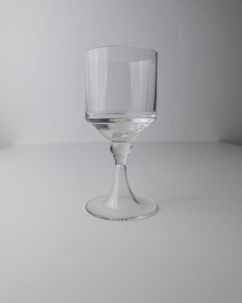 A clear vintage wine glass from the Bottega Jacobs 4 Classic Wine Glasses, Italy 70s set features a short stem and wide bowl, resting on a white surface against a light gray background.