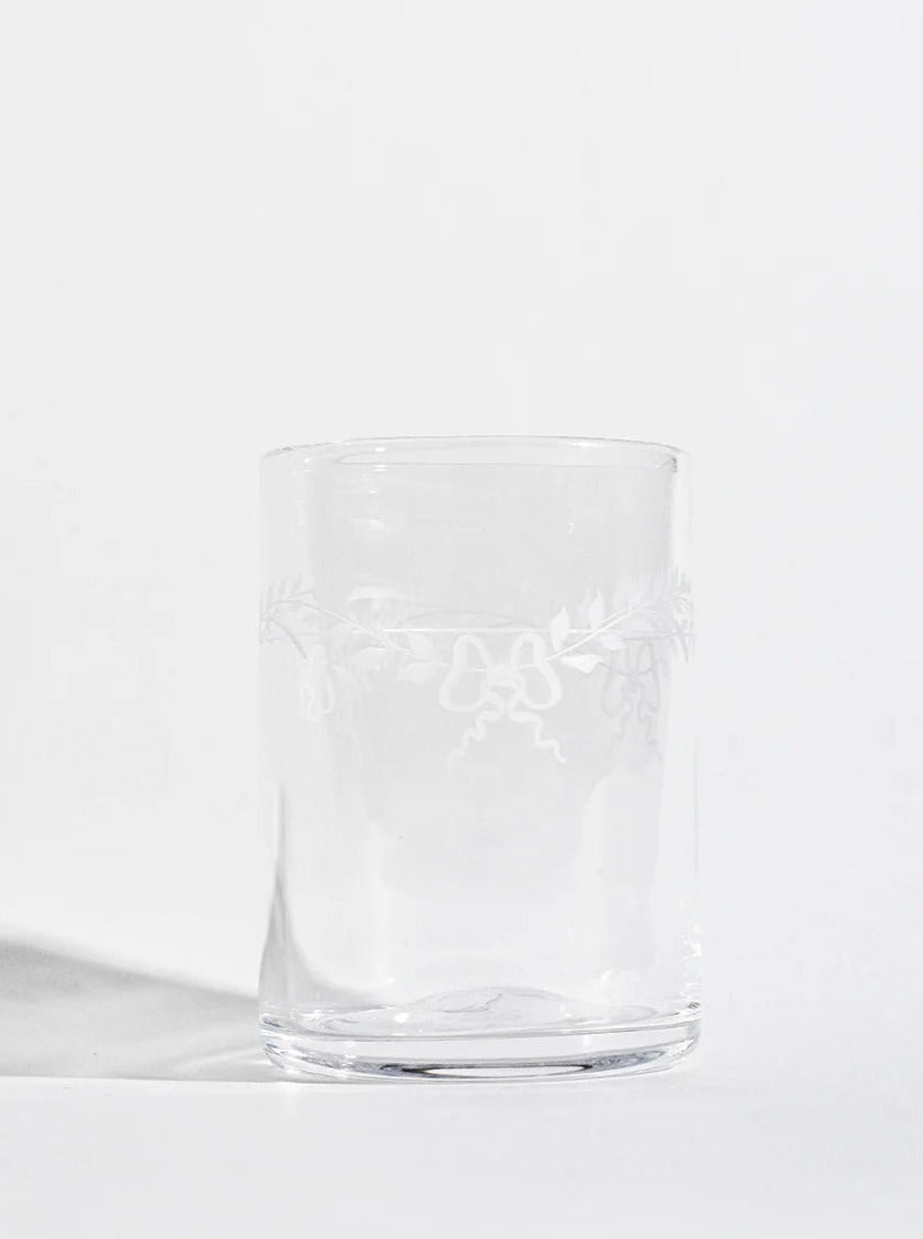 An empty Barbro Water Glass from Akua Objects with delicate floral patterns, set against a plain, light grey background with soft shadows.