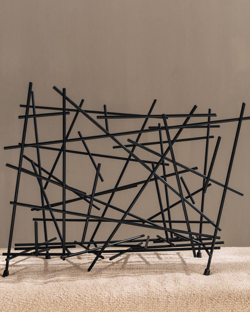 Black metal wire magazine rack with intersecting geometric structure by Alessi