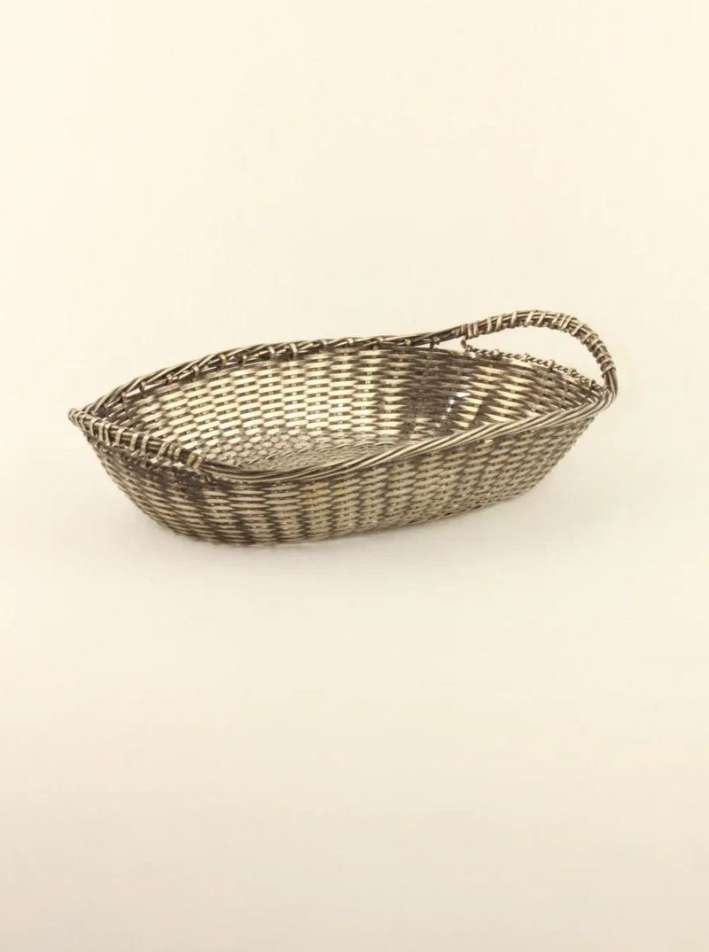 A shallow, oval-shaped hand-woven basket from Boga Avante Shop features a single handle on one end. Its intricate geometric pattern adds character, and it's displayed against a plain, off-white background.