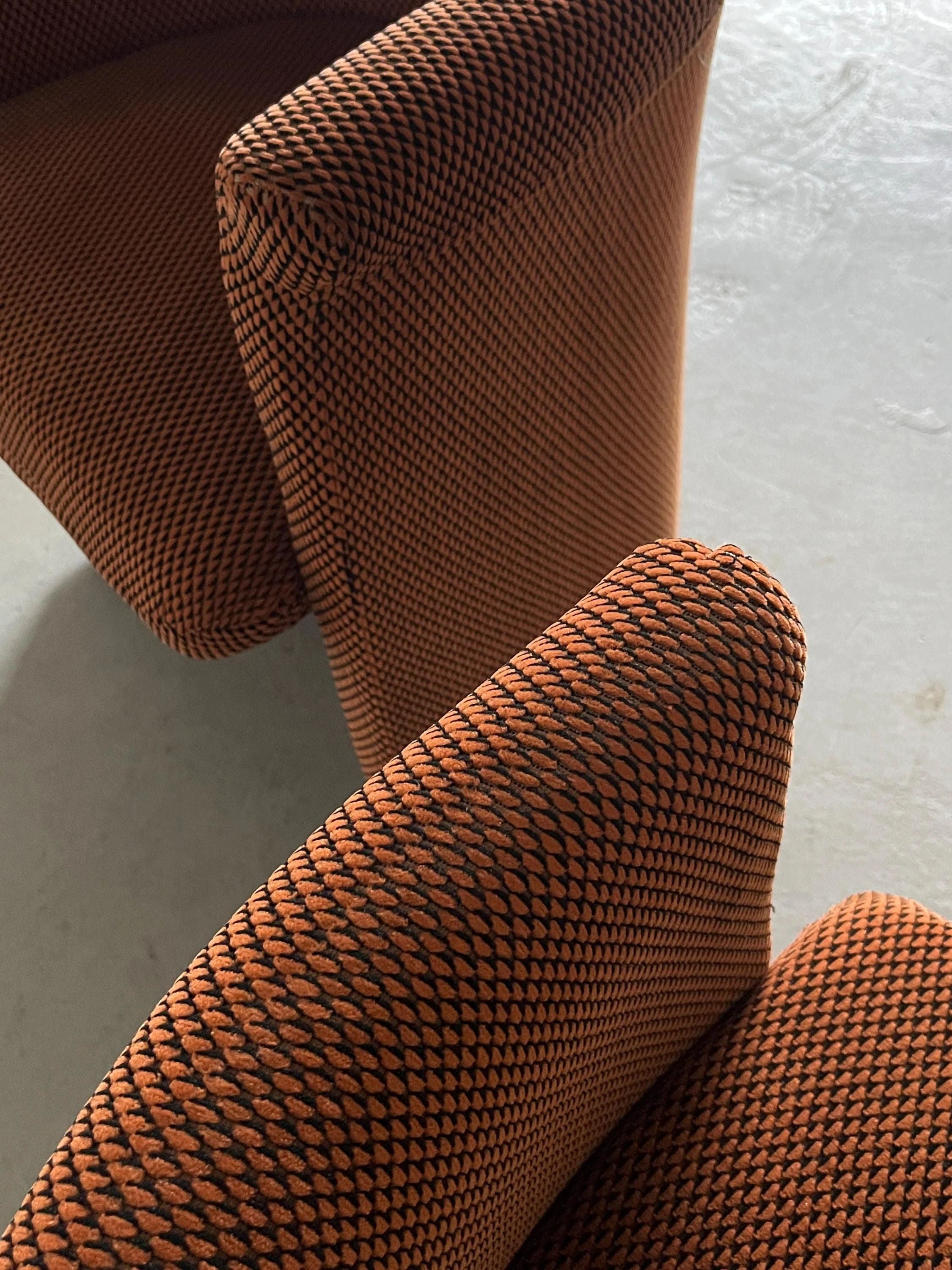 Close-up of Cherry Cargo's orange Postmodern armchairs with black diamond patterns on textured fabric. Facing each other on a light floor, sunlight highlights their vintage condition and enhances the fabric’s texture.