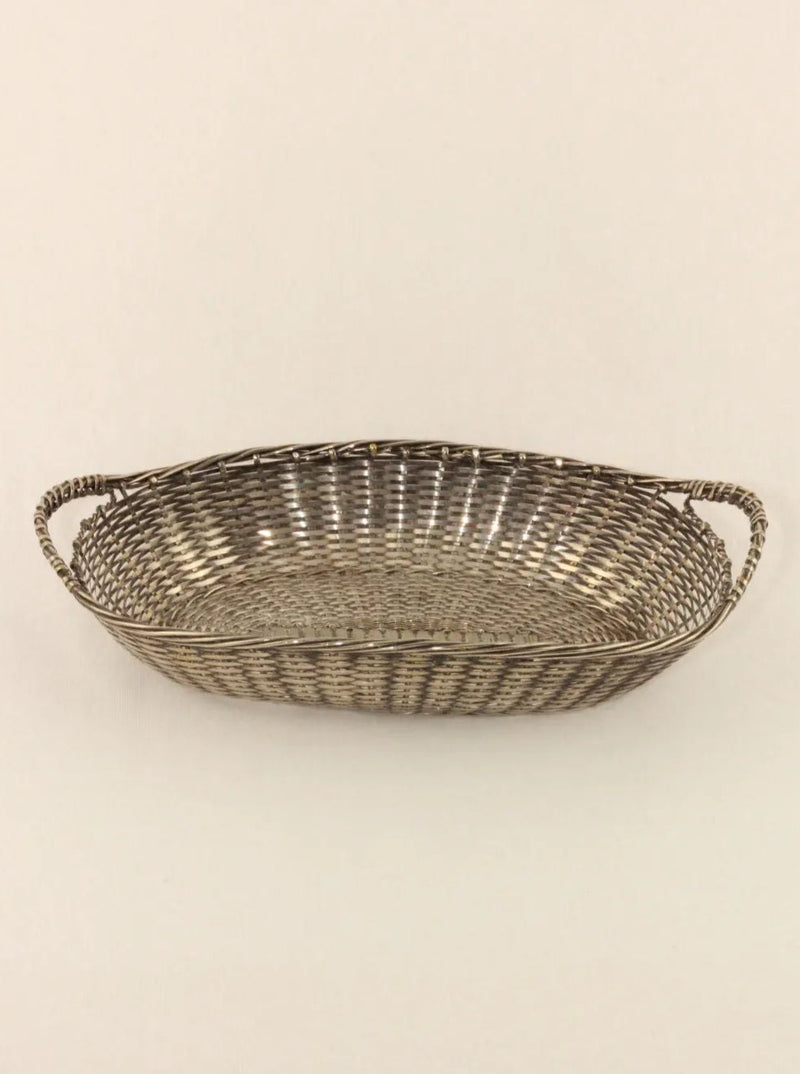 A shallow, oval-shaped hand-woven basket with braided handles on either side is displayed against a plain beige background. The Woven Basket by Boga Avante Shop, woven in a tight, uniform geometric pattern, exudes simplicity and elegance.