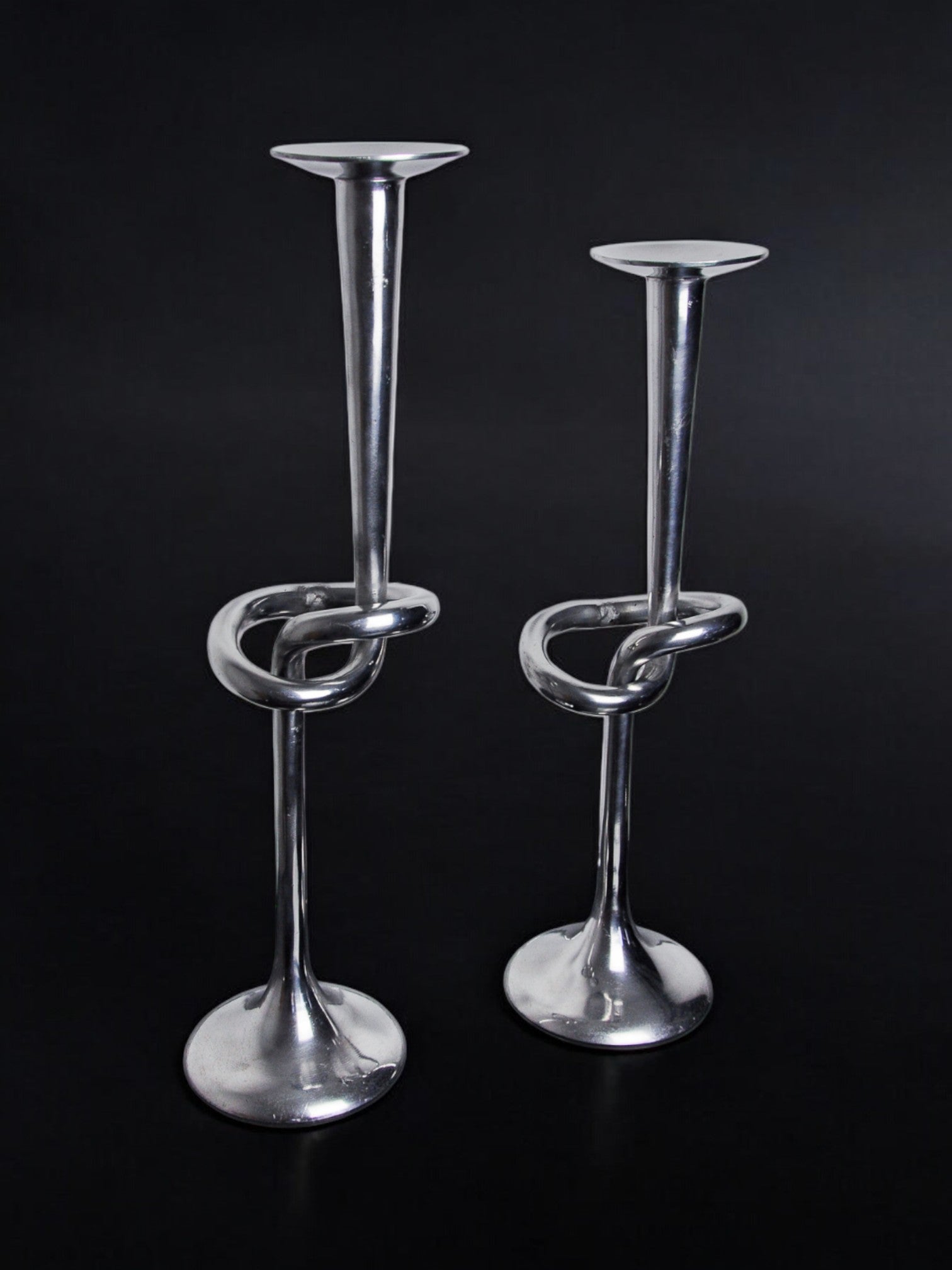 This Pair of XL knotted candlesticks by Malamar Studio (Italy, 1980) features twisted aluminum designs—one taller than the other—offering a striking modern touch to your decor.