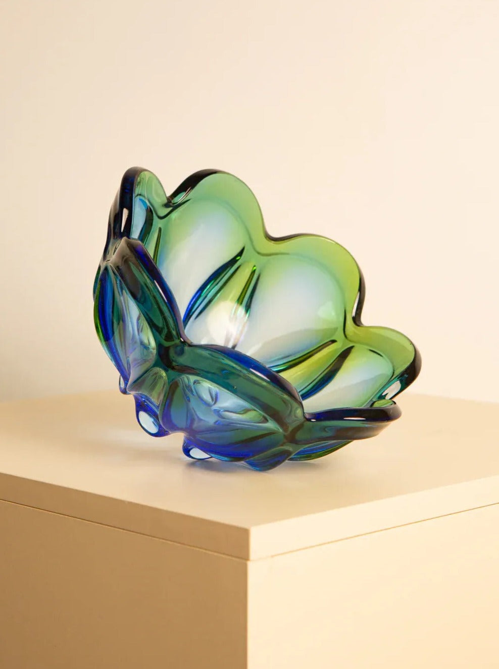 A large vide-poches "Flower" in 60's Murano glass by Treaptyque is displayed on a beige surface against a plain, light-colored background. The bowl, reminiscent of 1960s retro design, features a wavy, abstract shape with petal-like edges, showcasing exquisite Italian craftsmanship.