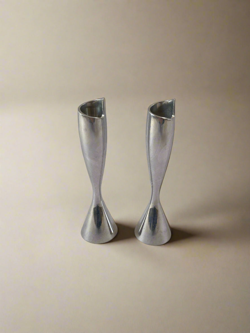 Two sleek, chrome candleholders with elegant hourglass shapes stand side by side against a plain, light-gray background. These Maud Vaughan Stylish Pair of Postmodern Chrome Candleholders add a touch of sophistication to any setting.