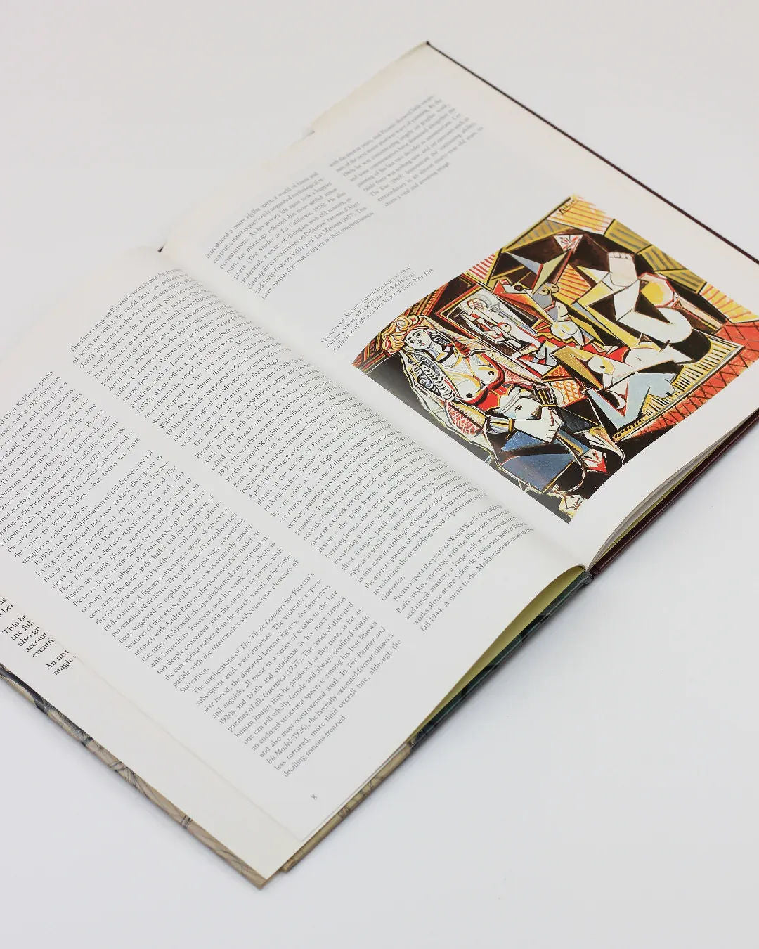 The open book, titled "Picasso by Gabriel Potter Vintage Art Book" from Boga Avante Shop, reveals two pages. The left side showcases dense black text, while the right presents an abstract colorful illustration echoing Picasso's modern art style with geometric shapes and figures, set against a white background.