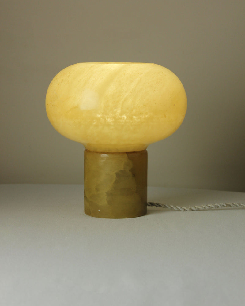 Golden alabaster table lamp with cylindrical base and dome shade illuminated