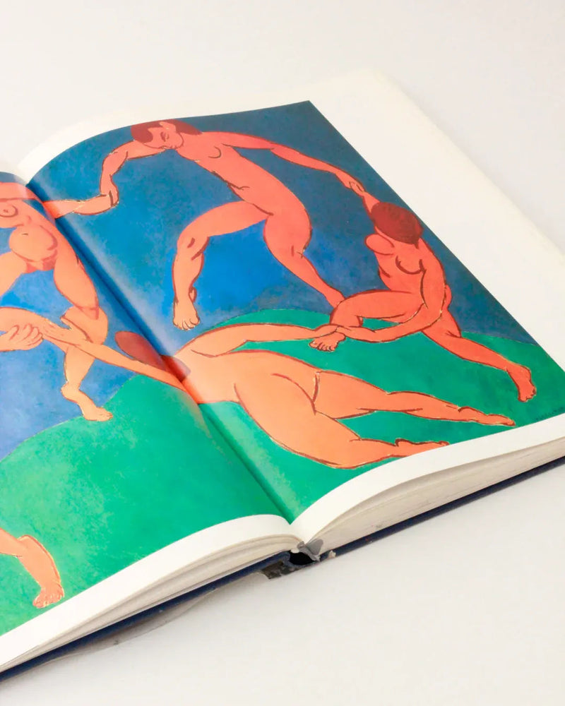 A book from Boga Avante Shop's Henri Matisse Vintage Book - Illustrated Publication lies open to a two-page spread featuring a colorful artwork by Matisse. The painting displays five nude figures in dynamic poses, holding hands in a circle against a blue and green background. Reminiscent of Matisse's modern art style, the figures are rendered in vibrant red and orange hues.