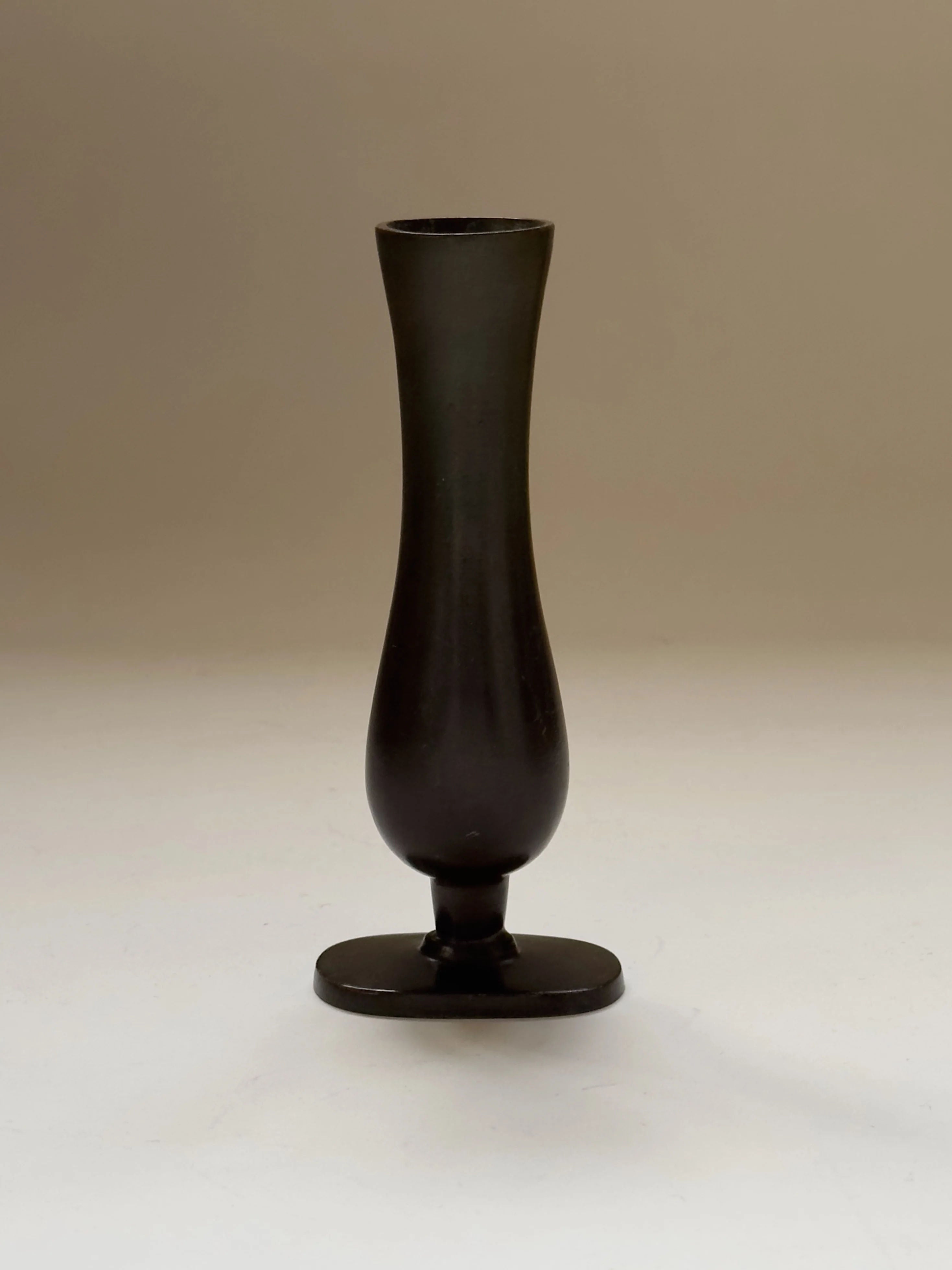 The GAB Bronze vase by Galerie Storm is a tall, narrow vase with a bulbous base and flared top, evoking Art Déco elegance. Its dark bronze finish stands out on a small square platform against a neutral background, capturing the understated sophistication of Swedish Grace.