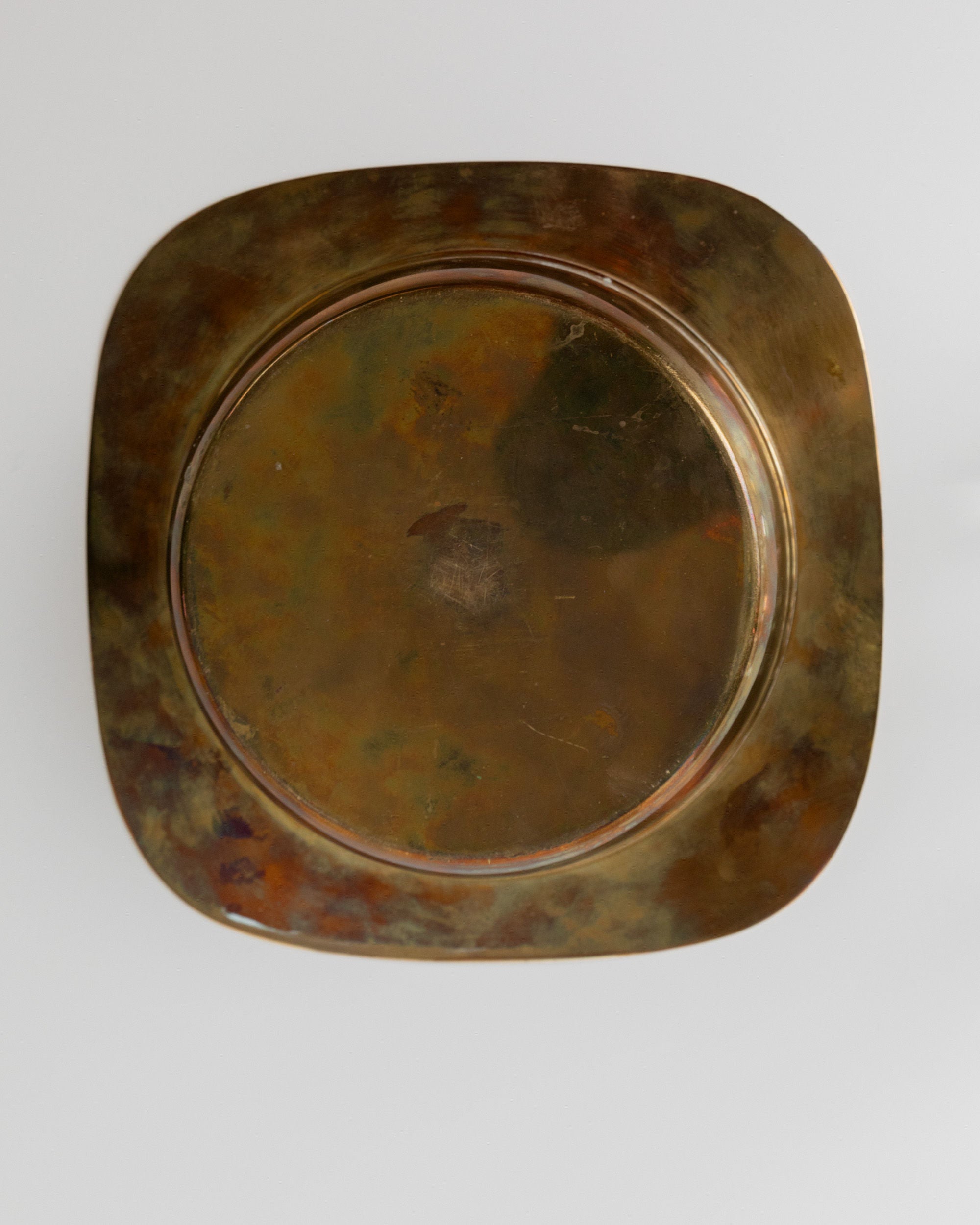 A tarnished, square copper plate with rounded edges is set against a light gray background. Its oxidized dark browns and greens give a vintage look, reminiscent of the Set Shot Glasses and Tray - Mid Century Design 70s by Bottega Jacobs, making it a charming decorative piece.