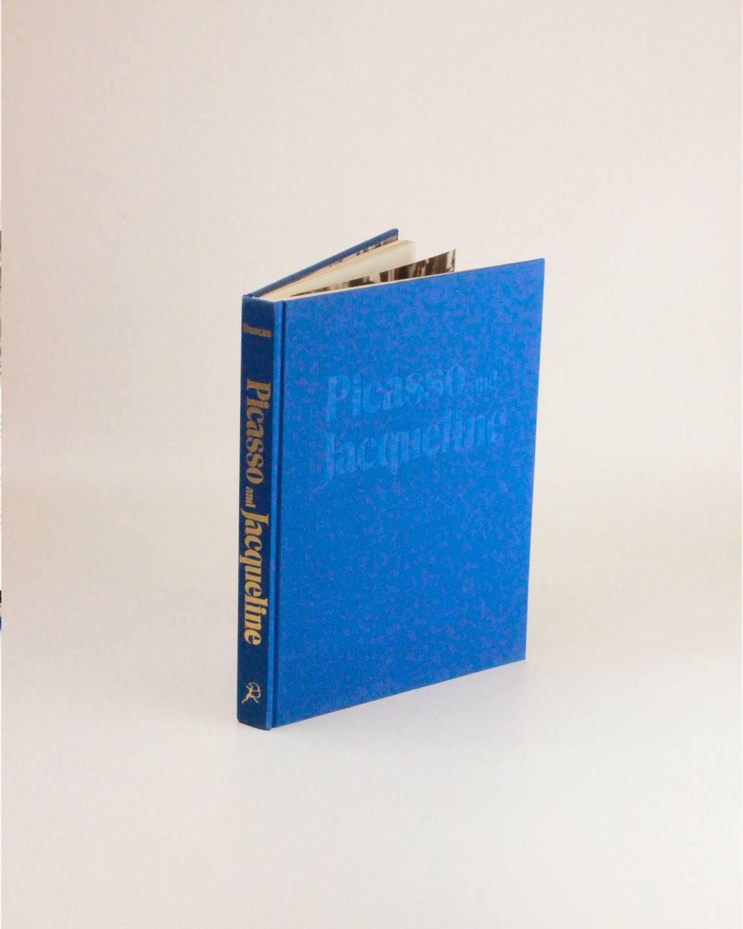 A blue hardcover book titled "Picasso and Jacqueline" from Boga Avante Shop stands upright, slightly open, against a plain white background. The title is yellow on the spine and embossed on the cover, showcasing David Douglas Duncan’s reflections.