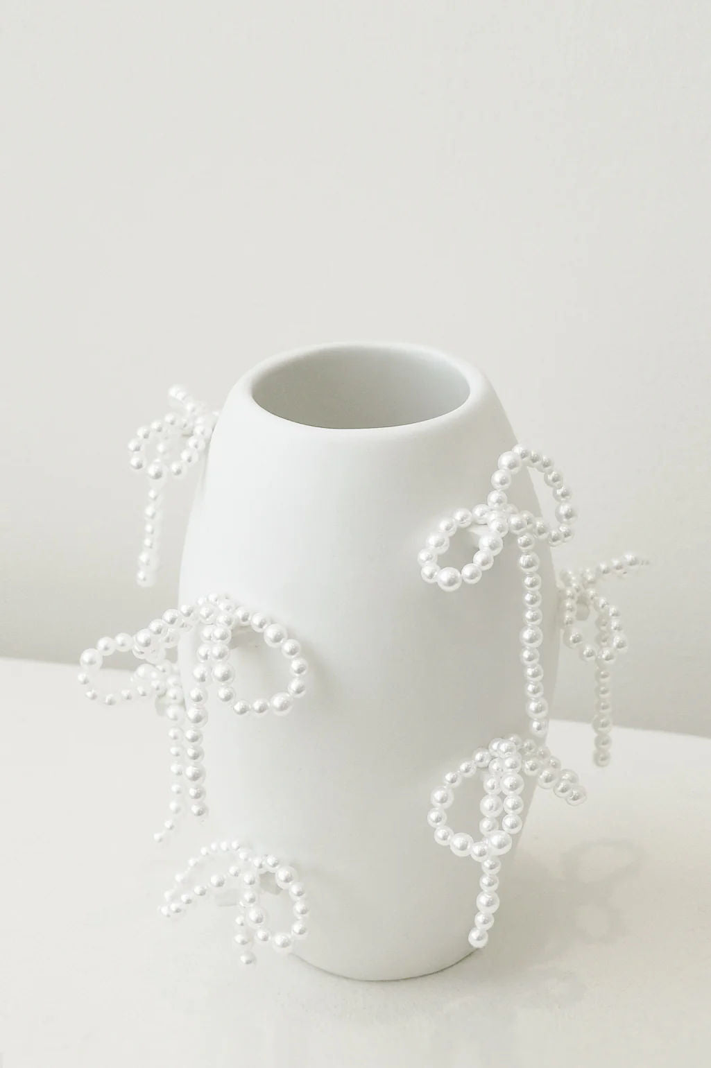 The "Notsobig" Small Vase in Matte White by Completedworks features a sculptural form with delicate white bead bows on its exterior, set against a light gray background.