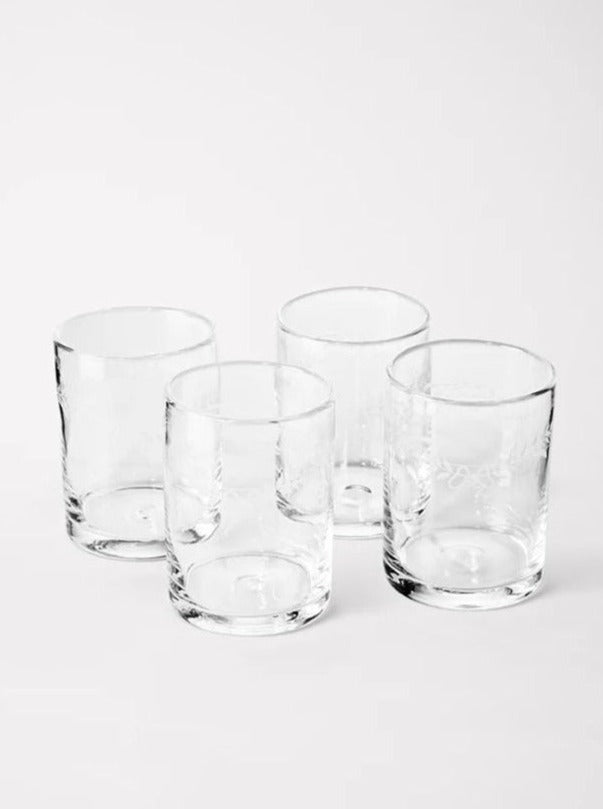 Four empty clear Akua Objects Barbro Water Glass Large - Set of four on a white background, with subtle shadows and light reflections on the glass surfaces.