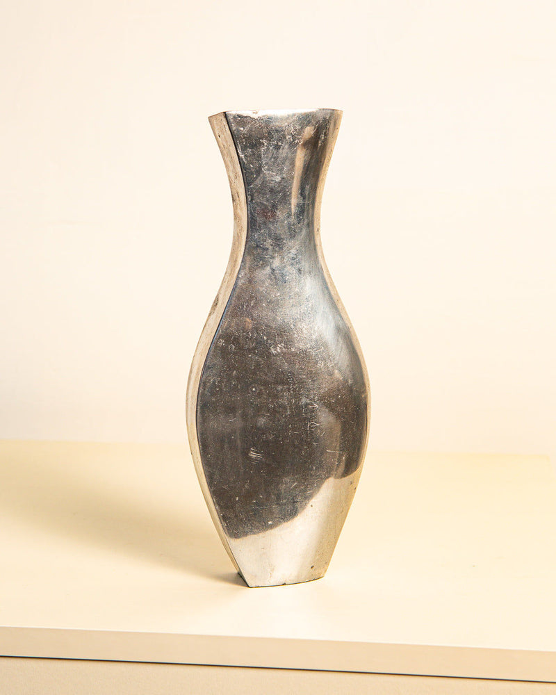 The Italian Vase "Dame" in Cast Aluminum 80's by Treaptyque, with its tall, reflective surface and minimalist design, features a narrow neck and subtly flared base. It exudes elegance against a light-colored surface reminiscent of Italian sculpture.