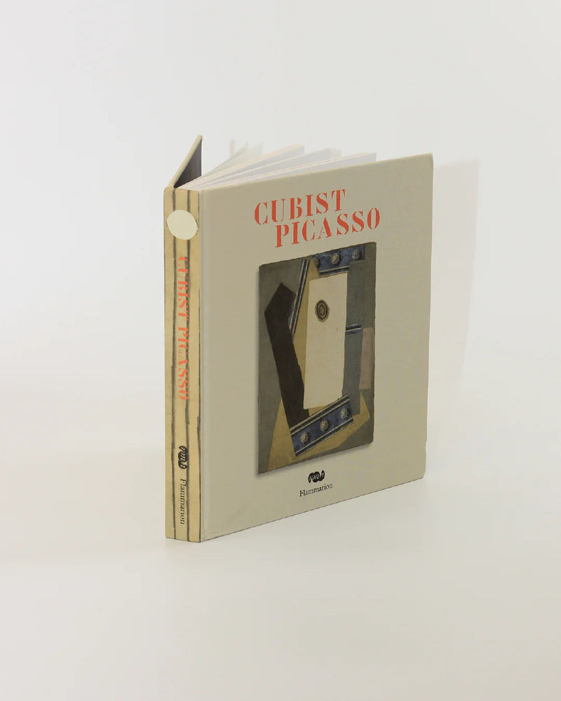 A hardcover book titled "Cubist Picasso Book" from Boga Avante Shop stands upright, slightly open. The cover showcases striking Cubism artwork comprised of geometric shapes, with the title and the publisher's logo on the spine, encapsulating Pablo Picasso's groundbreaking artistic vision.