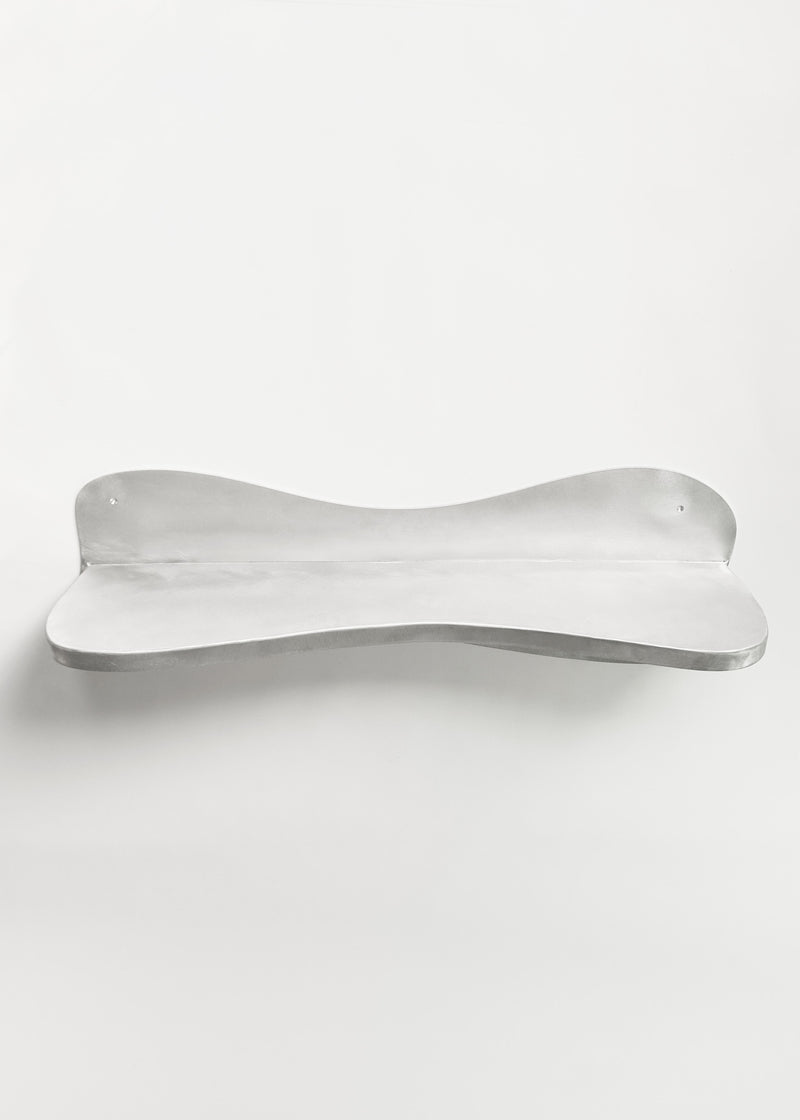 The handcrafted Big Shelf by Six Dots Design is a wall-mounted, minimalist piece made of sturdy metal with a gently curved design. Its silver finish reflects light for a sleek, modern look against a white background, creating a curated focal point.