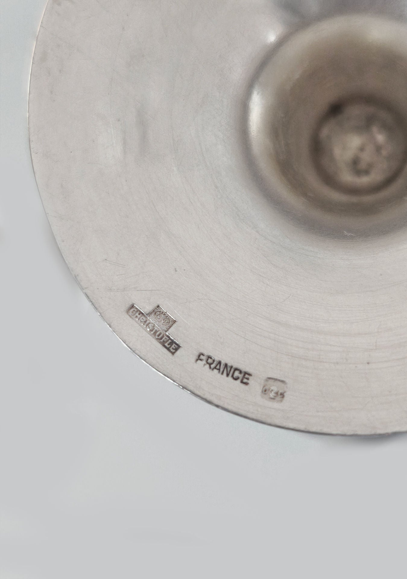 This close-up of a metallic object with engravings embodies timeless luxury. The Les Objoies logo reads "Christofle" and "France 65," hinting at its origin. Its silver-plated surface appears slightly scratched, with a smooth concave center, ideal for elegant home decor.