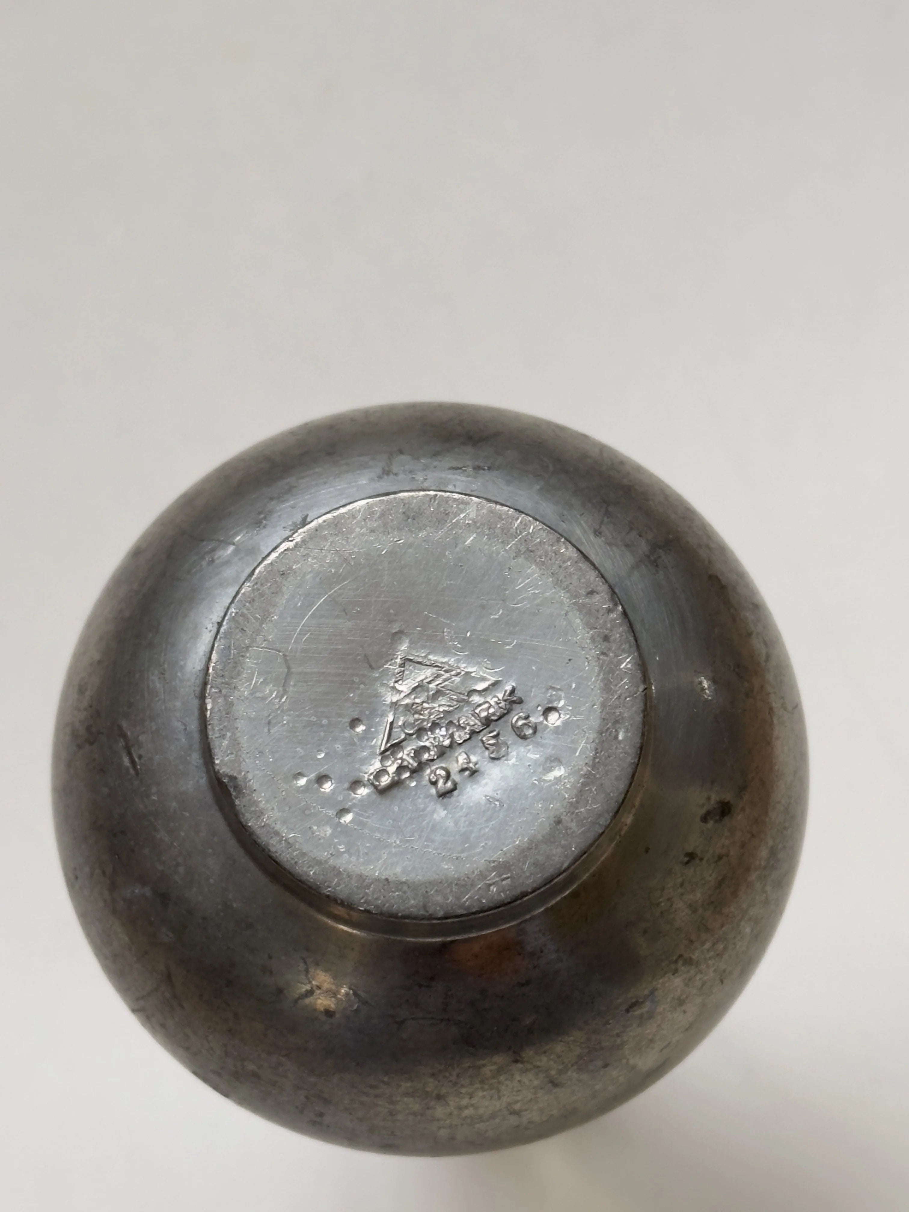 The bottom view of the Just Andersen Pewter Vase by Galerie Storm reveals a circular base with an embossed triangular logo, small text, and "2966" beneath it. This decorative vase features a smooth, polished surface that highlights its exquisite craftsmanship.