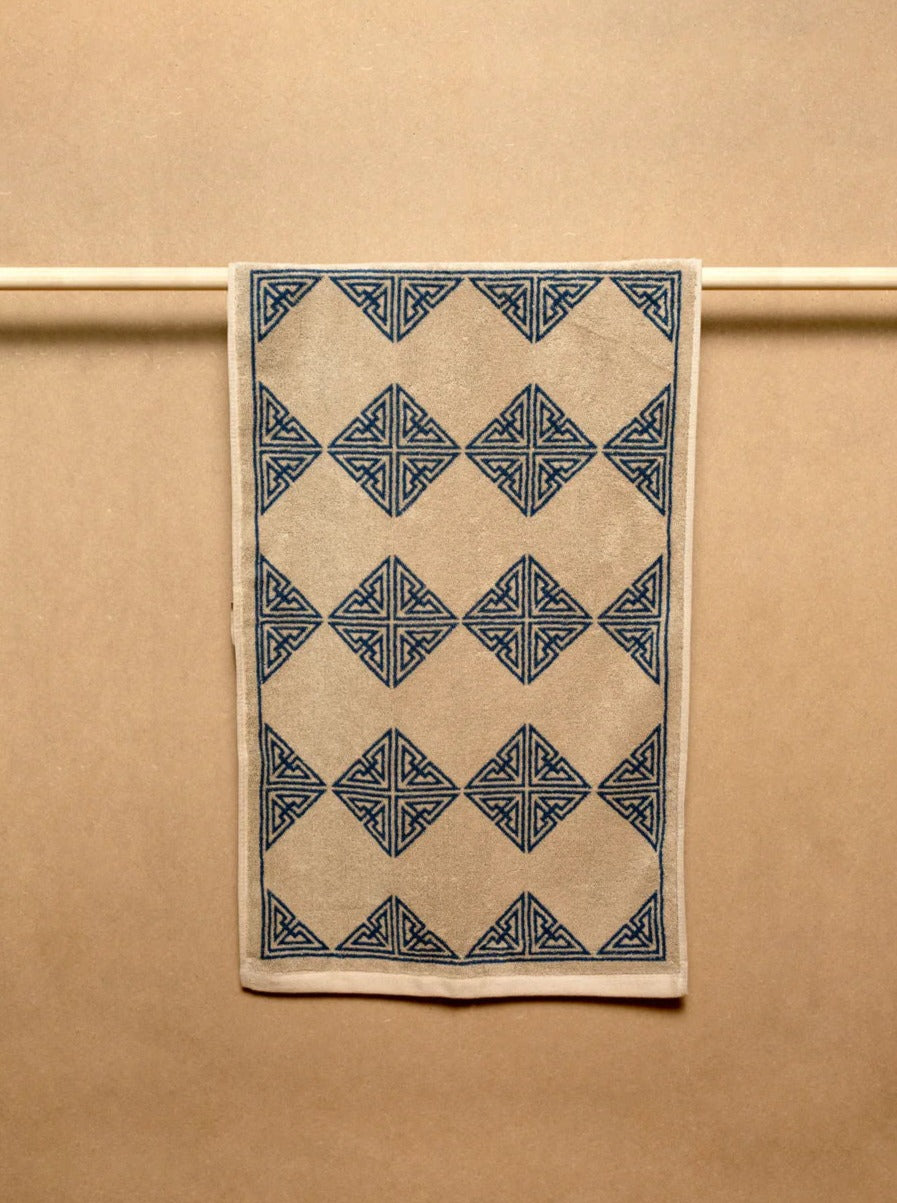 A rectangular vintage rug with intricate marine blue geometric patterns hangs against a plain beige background.