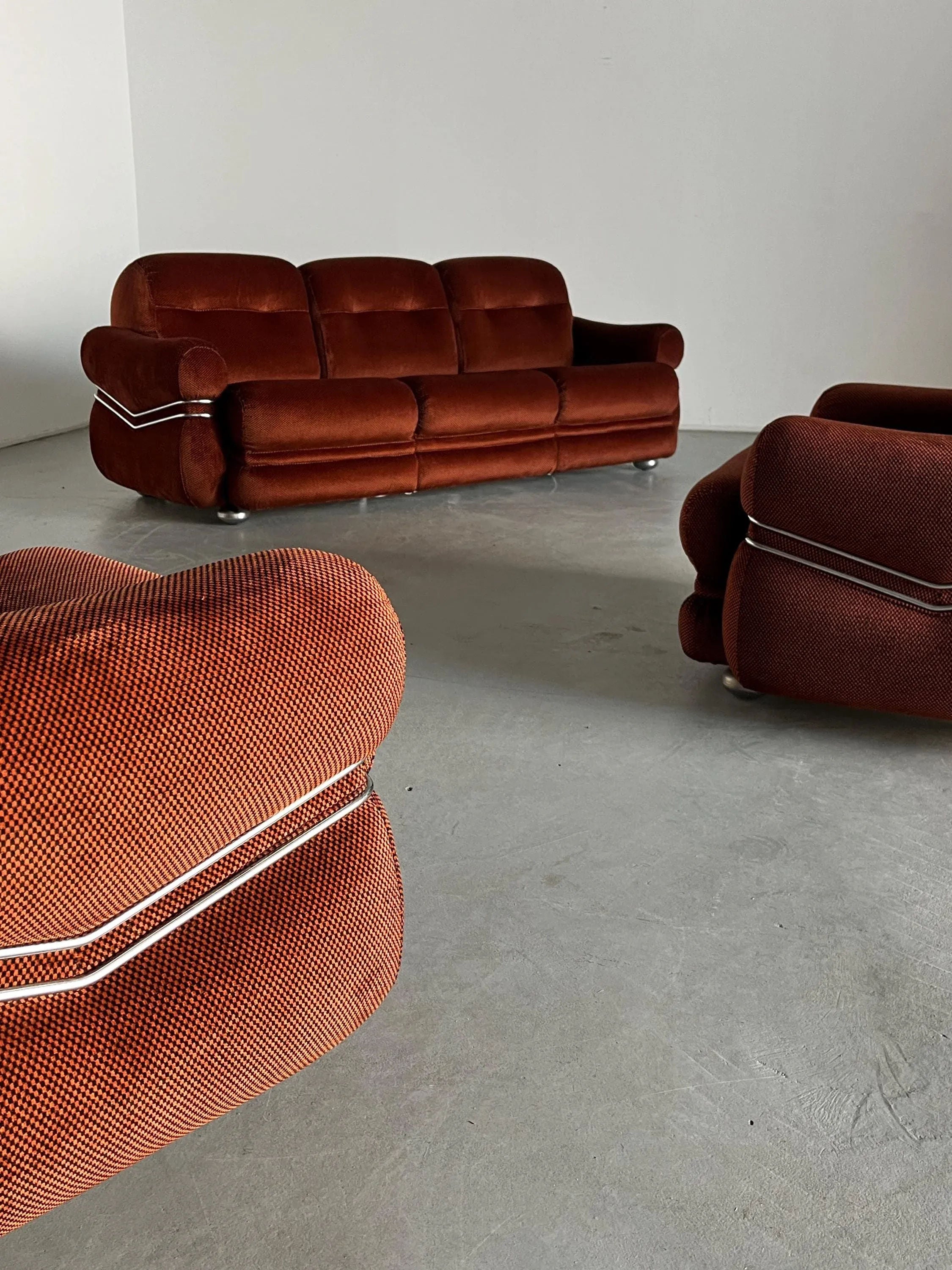 A Cherry Cargo Italian Space Age Seating Set from the 1970s, featuring checkered upholstery, complements the minimalist room's light gray floors and white walls. This vintage piece comprises a three-seater sofa and two armchairs with curved designs and elegant white piping.