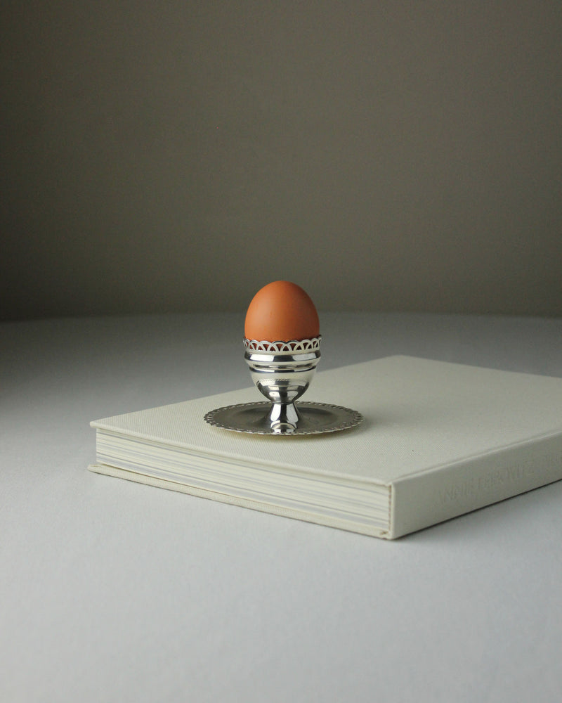 Silver egg cup with decorative rim holding brown egg on white books