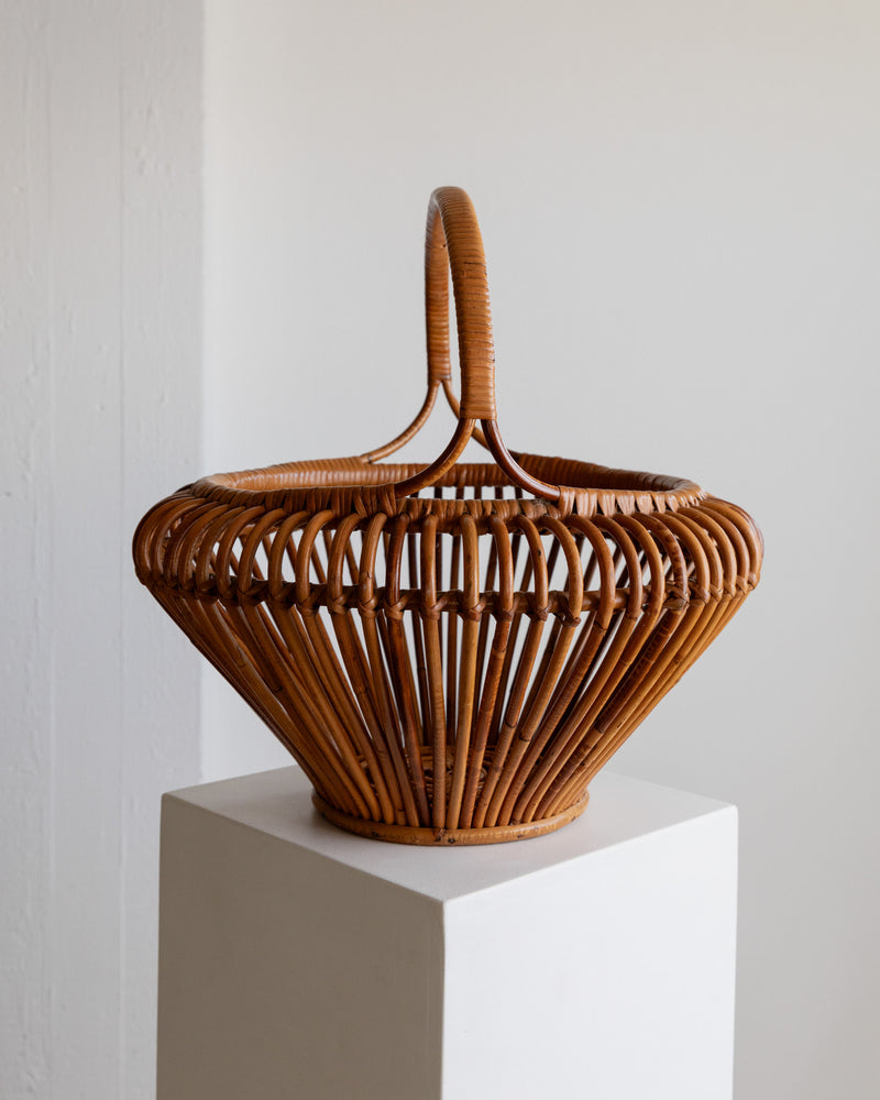The XL Vintage Bamboo Basket from Bottega Jacobs features a curved handle and geometric open-weave design, exuding mid-century flair on a white pedestal with a light neutral background—an ideal retro gift.