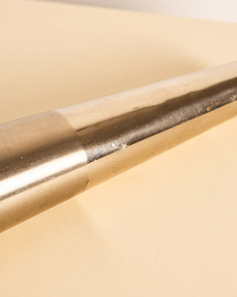 A close-up of Treaptyque's Metal Cone Vase 80s shows its vintage charm, polished metal finish, and narrow-to-wide cylindrical shape. It rests against a beige background with a slightly textured surface.