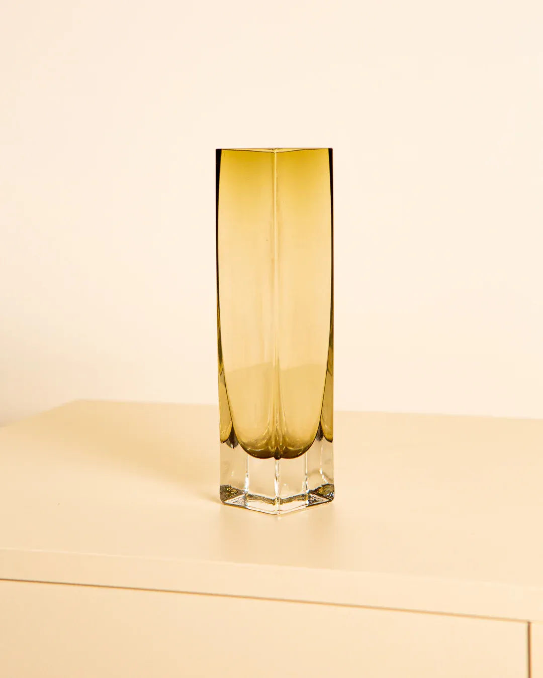 The 80's Murano Glass Amber Vase by Treaptyque, tall and translucent with an amber tint, stands on a light surface against a cream background, reflecting vintage elegance from Italian master glassmakers.