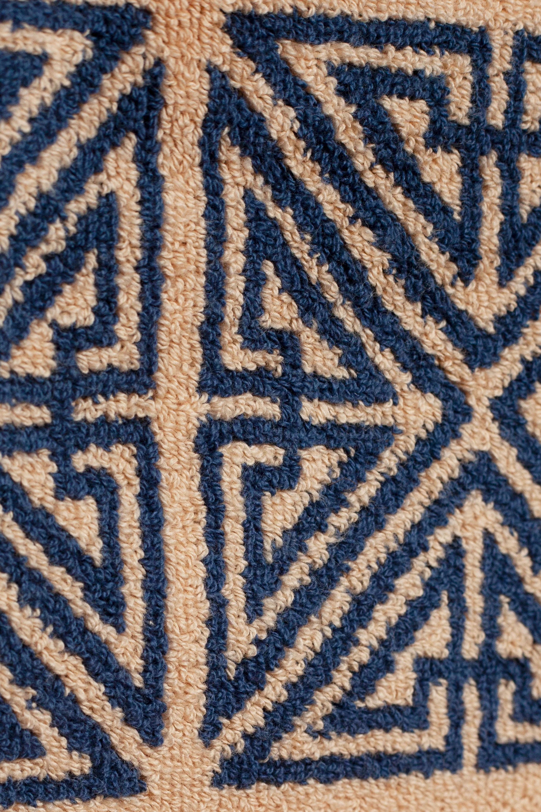 Close-up of an Autumn Sonata Agnes Bath Mat featuring intricate geometric patterns in marine blue and beige. The design includes sharp angles and intersecting lines, creating a detailed, symmetrical motif.